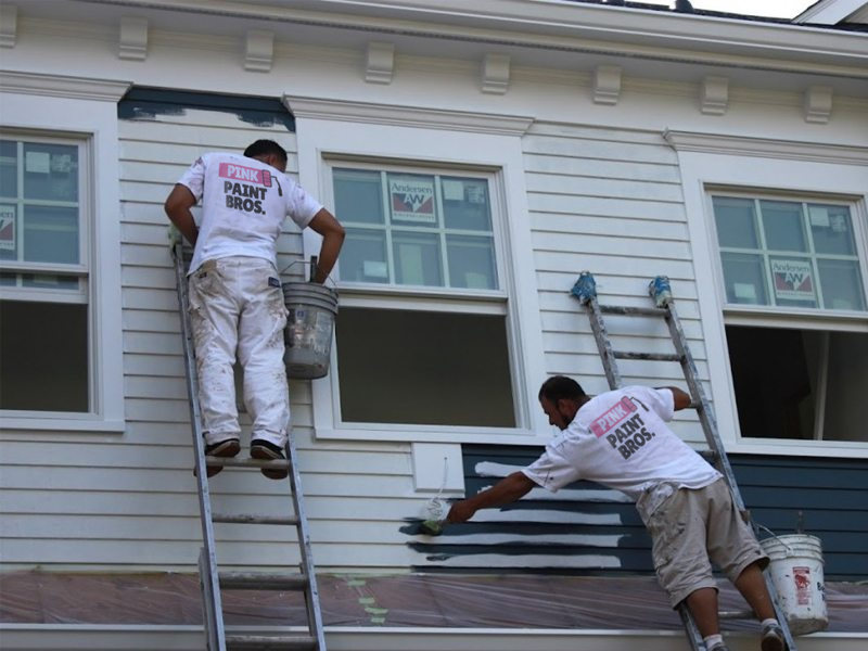 Two painters working on the siding of a house